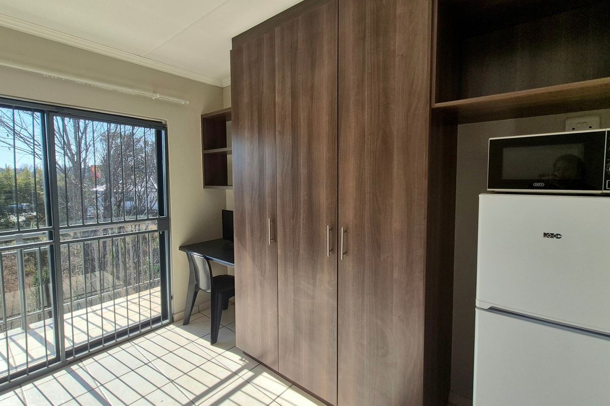 Bedroom featuring built-in wooden cupboards, tiled flooring, and a sliding glass door with security bars leading to an outdoor area.