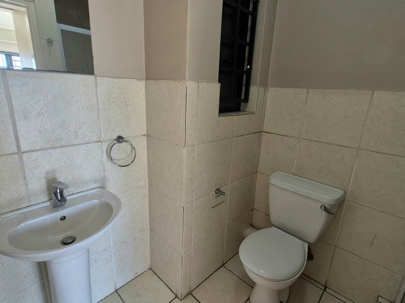 A compact bathroom featuring a pedestal washbasin, standard toilet, and neutral wall and floor tiling with security bars on the window.
