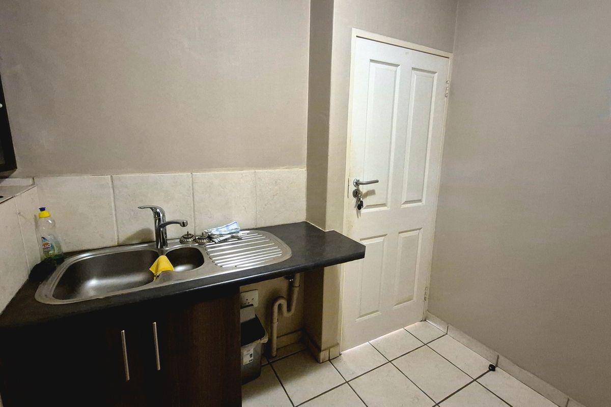 A functional scullery area featuring a stainless steel sink, laminate countertop, tiled splashback, and ceramic floor tiles.