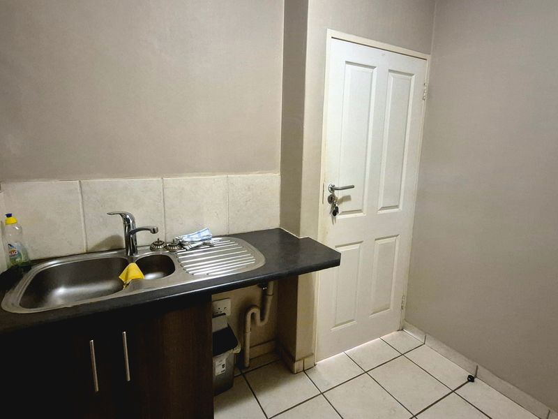 A functional scullery area featuring a stainless steel sink, laminate countertop, tiled splashback, and ceramic floor tiles.