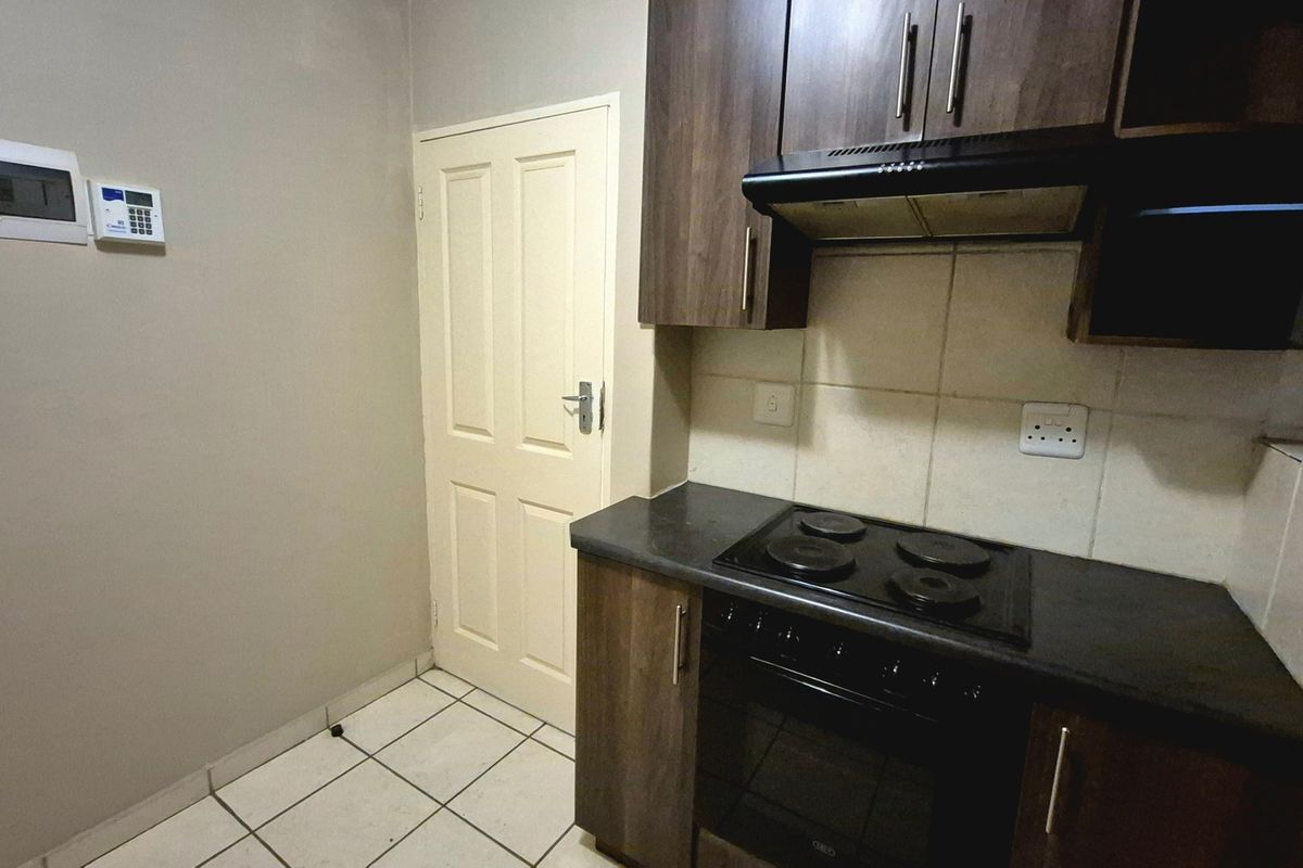 Compact kitchen featuring dark wood cabinetry, built-in electric oven and hob, extractor fan, and tiled flooring.