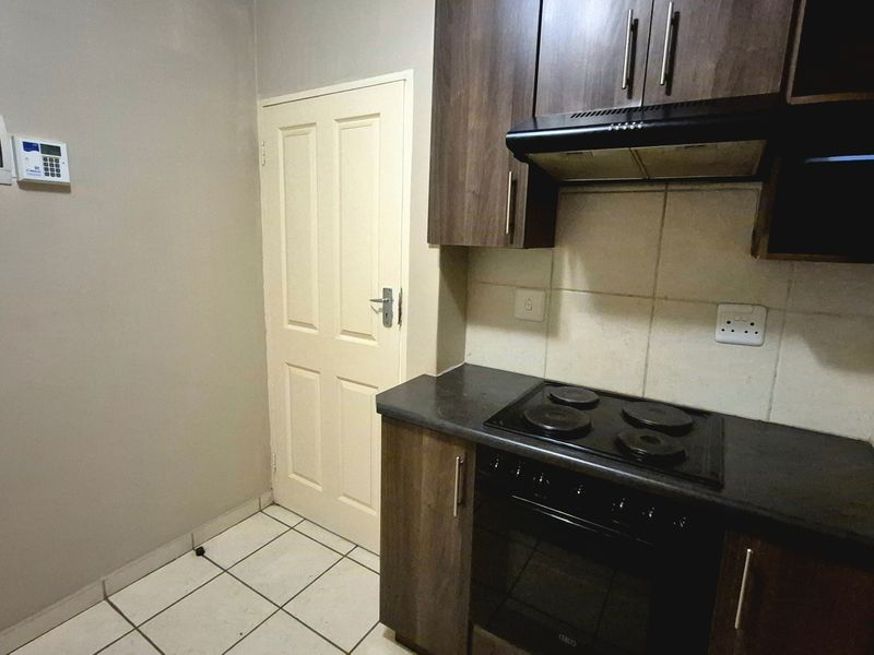 Compact kitchen featuring dark wood cabinetry, built-in electric oven and hob, extractor fan, and tiled flooring.