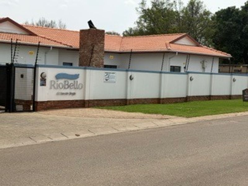 Street view of the property entrance featuring a secure perimeter wall with electric fencing, a brick chimney, and a tiled roof.