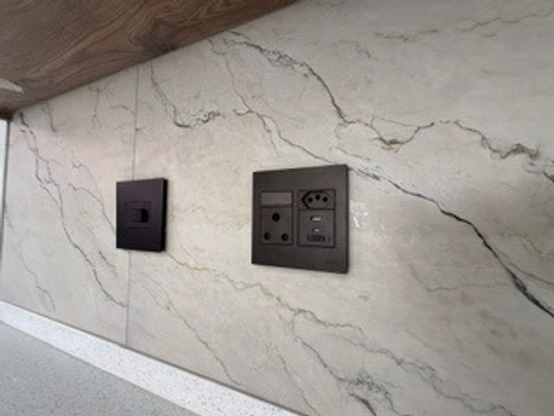 Close-up view of a modern kitchen splashback featuring marble-effect tiling, integrated electrical outlets, and a light switch.