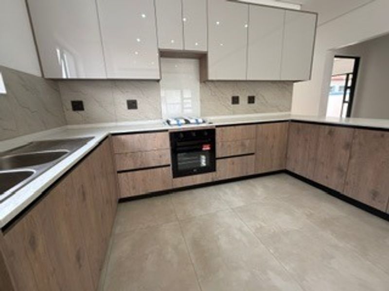 Modern kitchen featuring sleek two-tone cabinetry, stone countertops, integrated oven and hob, and neutral tiled flooring.