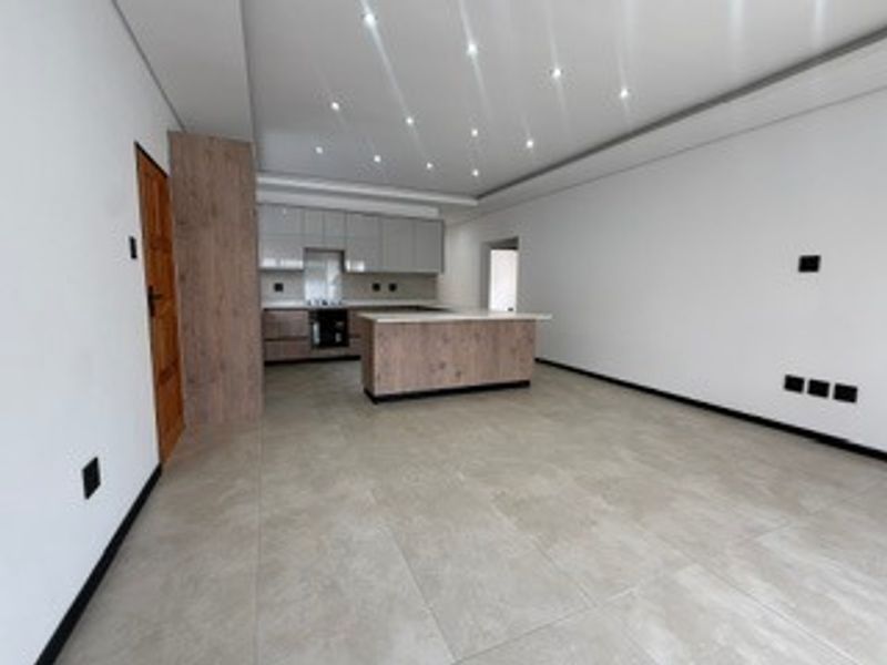 Modern open-plan living area featuring a contemporary kitchen with a central island, sleek cabinetry, and recessed ceiling lighting throughout.