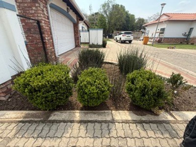 Front view of the property featuring a brick facade, garage door, and a well-maintained garden bed along the paved driveway.