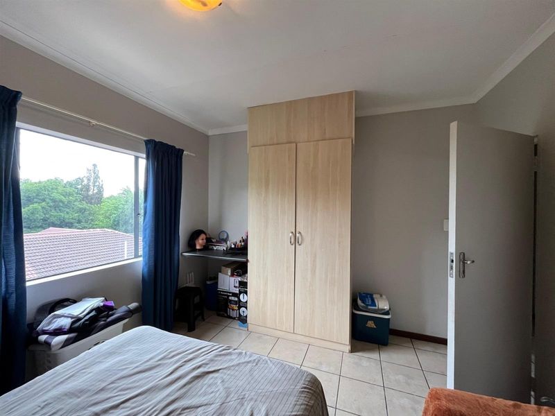 A bedroom featuring tiled flooring, a built-in wardrobe, and a built-in desk area with natural light from a large window.