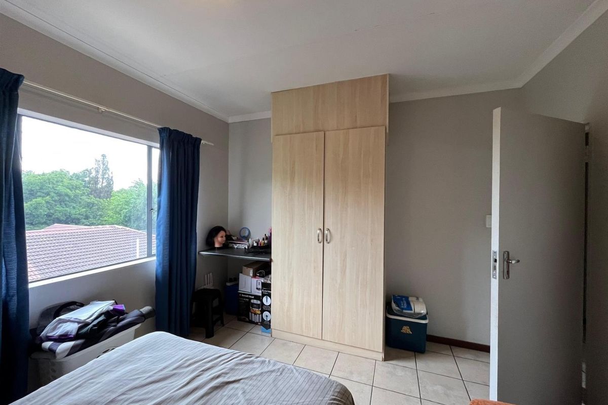 A bedroom featuring tiled flooring, a built-in wardrobe, and a built-in desk area with natural light from a large window.