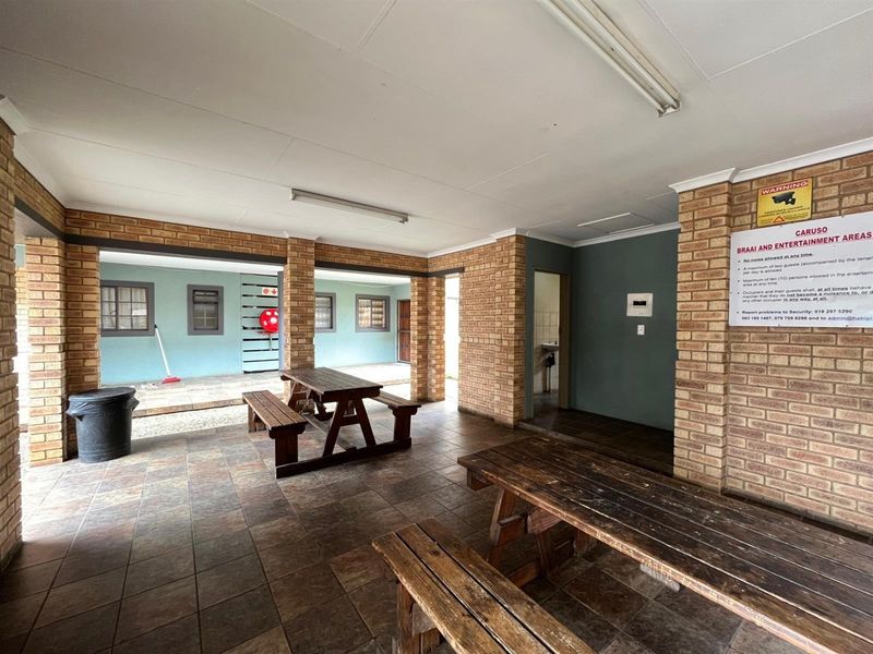 A covered outdoor entertainment area featuring face brick columns, tiled flooring, and communal seating space.