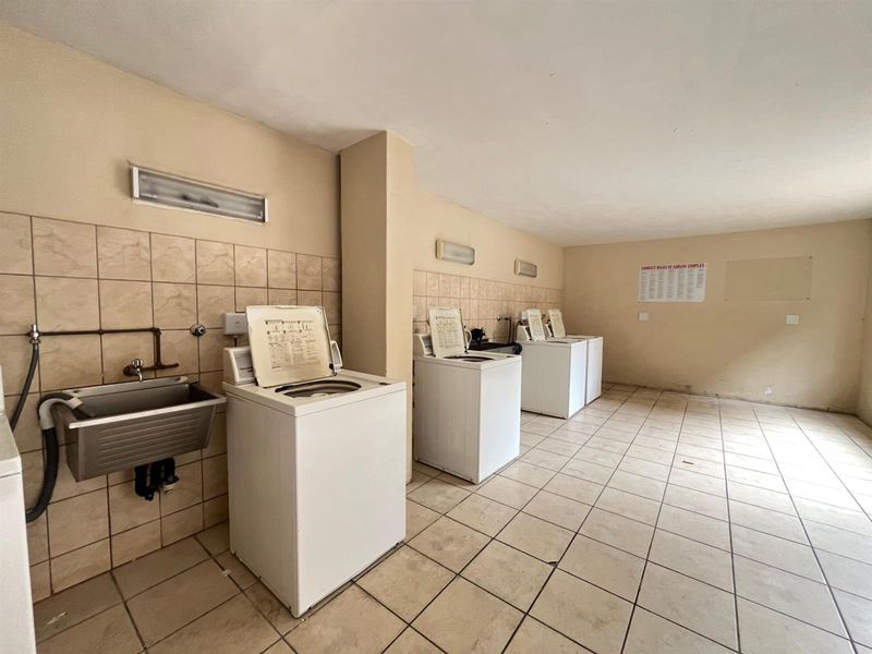 Communal laundry facility featuring multiple washing machine connections, a stainless steel utility sink, and tiled finishes throughout.