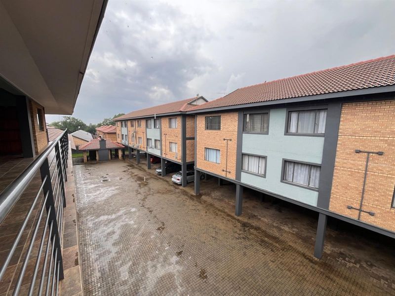 An elevated view of an apartment complex exterior featuring brick facades, tiled roofing, and a paved courtyard with covered parking areas.