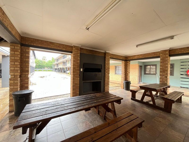 A covered outdoor patio area featuring brick pillars, tiled flooring, and a built-in braai, providing a functional space for outdoor dining and entertainment.