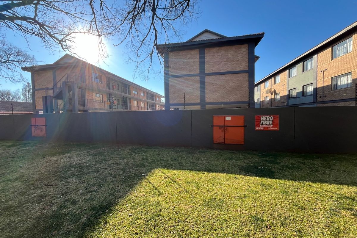 A view of the apartment complex exterior featuring a perimeter boundary wall, electric fencing, and brick building facades with external staircases.