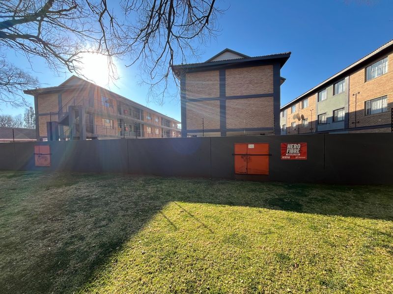 A view of the apartment complex exterior featuring a perimeter boundary wall, electric fencing, and brick building facades with external staircases.