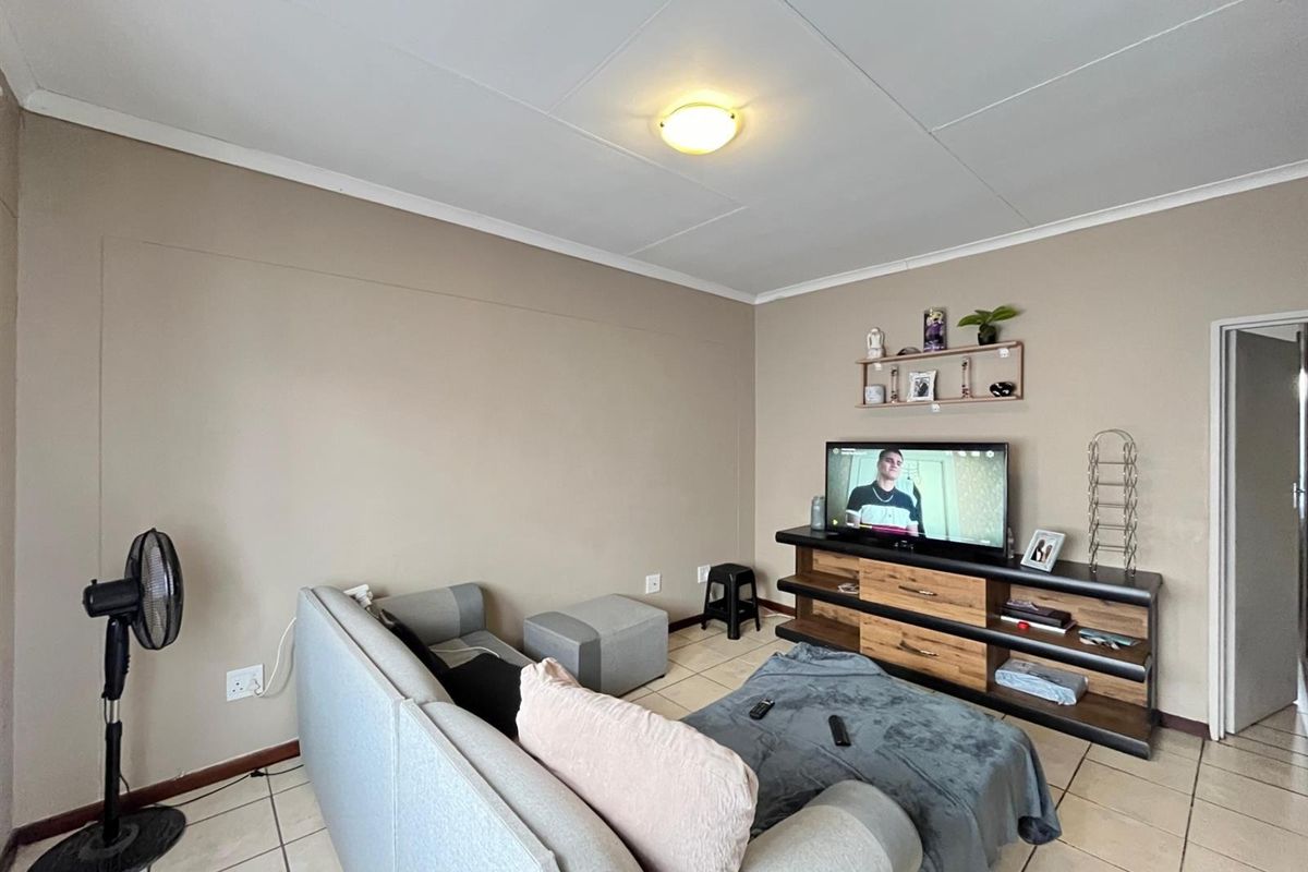 A functional living room featuring neutral wall tones, tiled flooring, and a standard ceiling light fixture, providing a comfortable and practical living space.