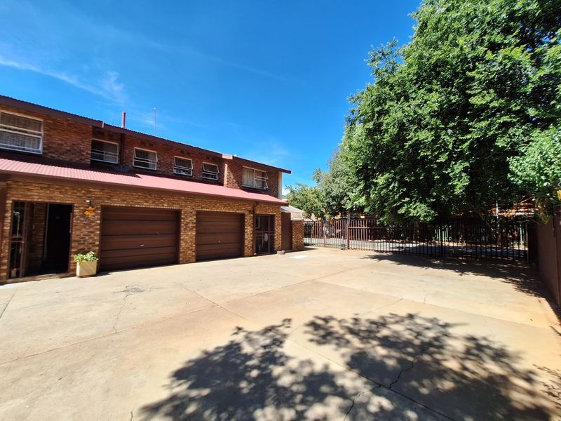 Front exterior view of a townhouse featuring a double garage, brick facade, and a paved driveway with perimeter security fencing.
