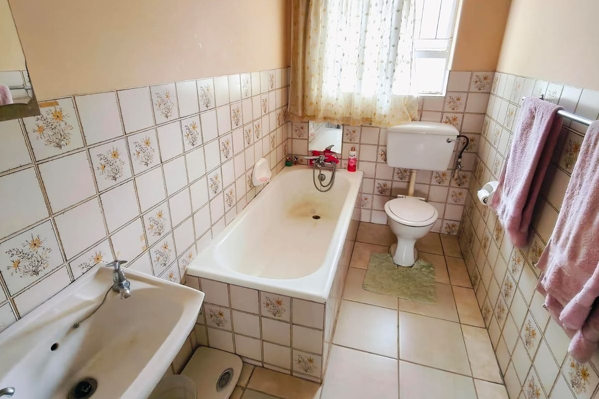 A dated bathroom featuring a built-in bathtub, pedestal basin, and toilet, finished with patterned ceramic wall tiles and neutral floor tiles.