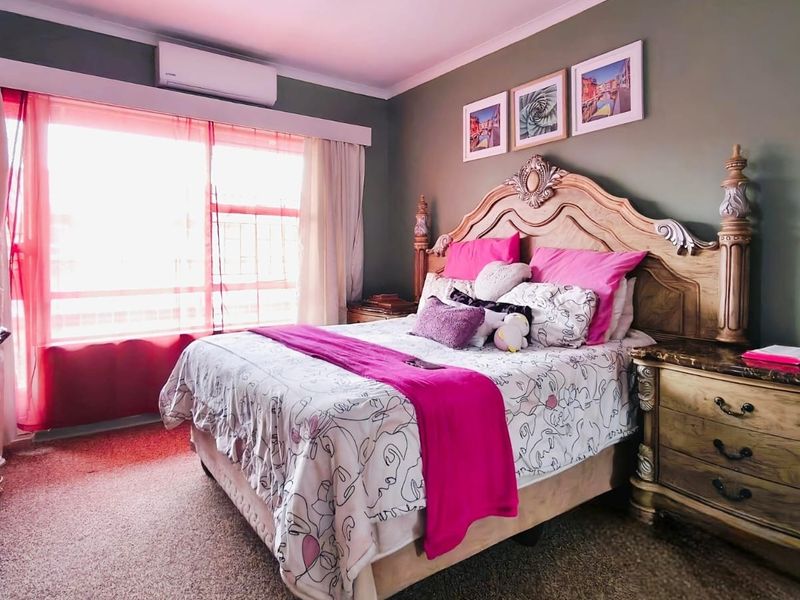 A well-lit bedroom featuring carpeted flooring, a wall-mounted split-system air conditioner, and large windows allowing for natural light.