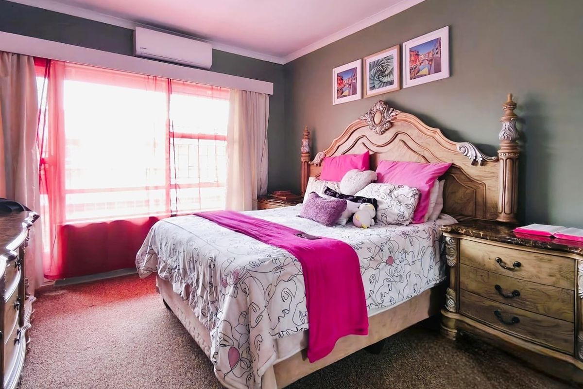 A well-lit bedroom featuring carpeted flooring, a wall-mounted split-system air conditioner, and large windows allowing for natural light.