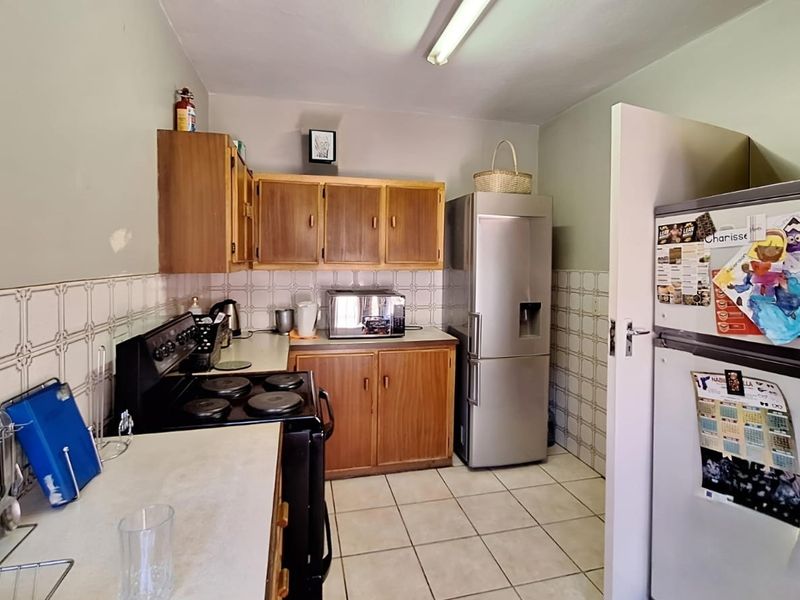 A functional kitchen featuring wooden cabinetry, tiled backsplash, and tiled flooring, offering a dated aesthetic with potential for modernization.