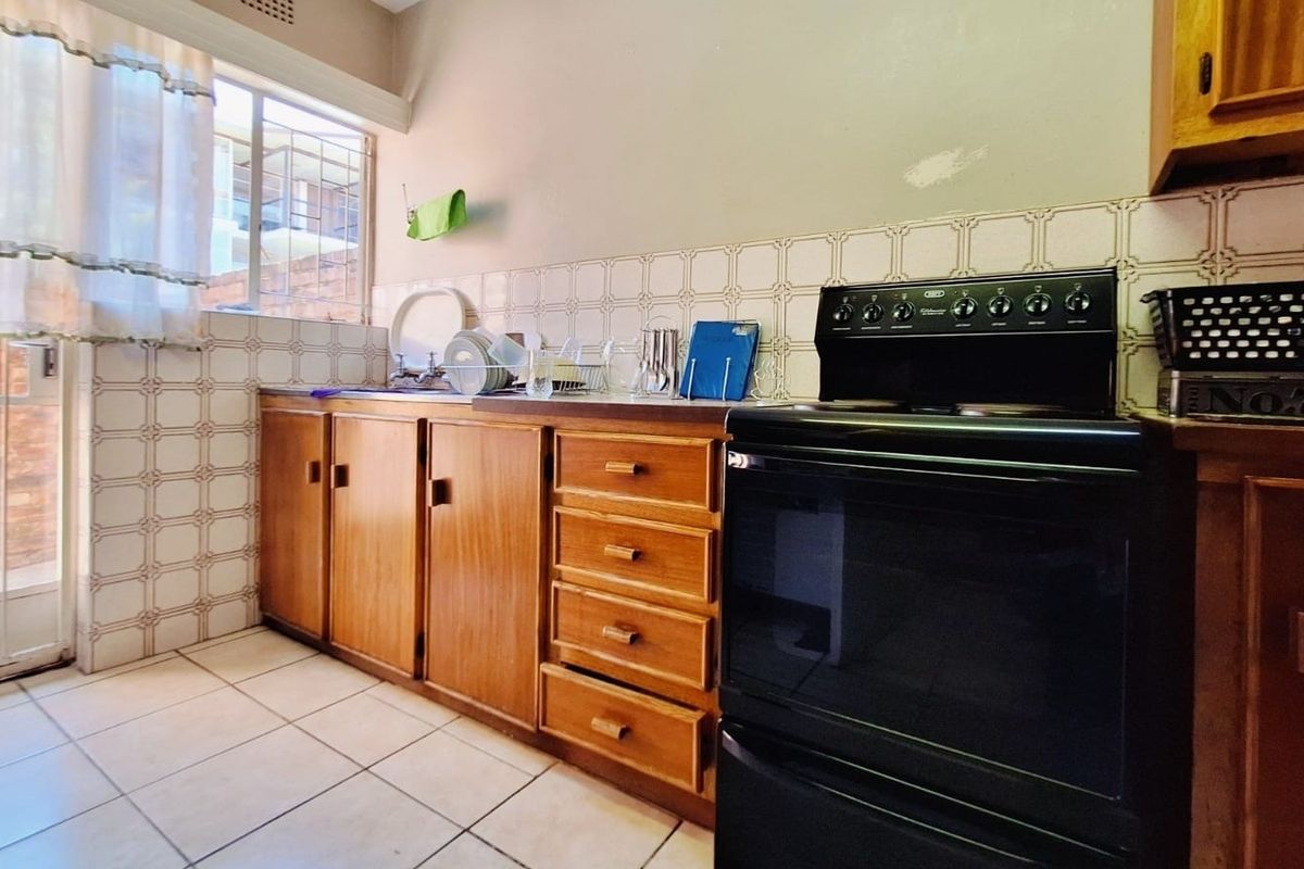 A functional kitchen featuring wooden cabinetry, tiled backsplash, and a freestanding stove, offering a dated aesthetic with potential for modern renovation.