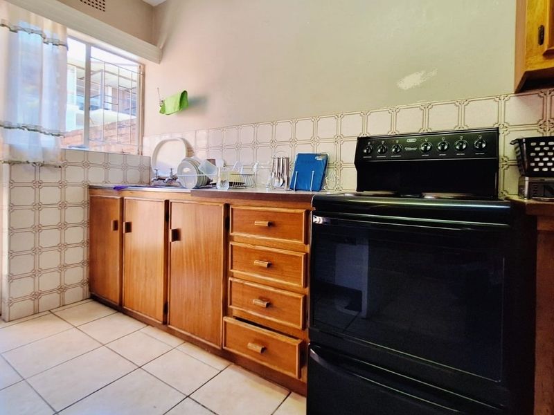 A functional kitchen featuring wooden cabinetry, tiled backsplash, and a freestanding stove, offering a dated aesthetic with potential for modern renovation.