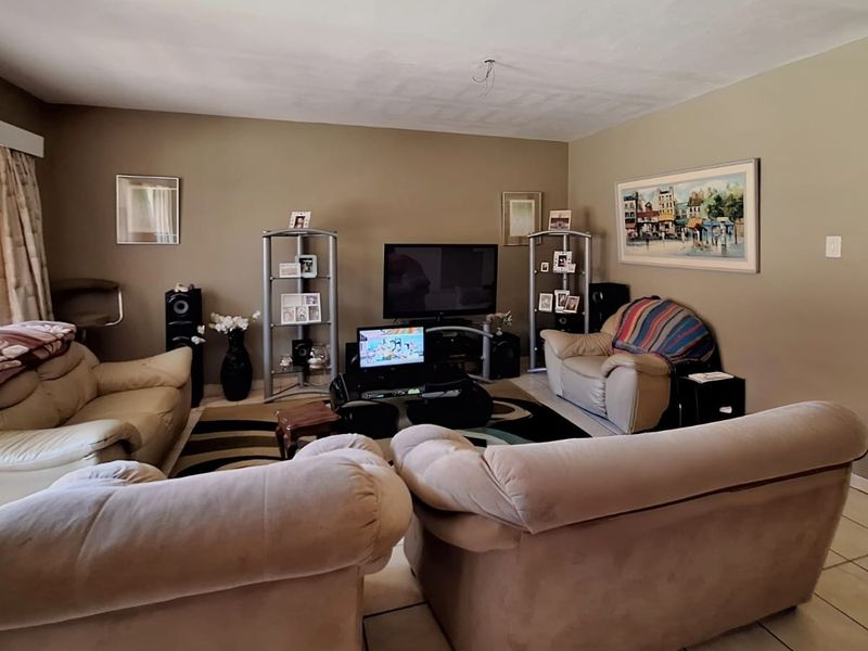 A spacious living room featuring neutral wall tones and tiled flooring, with an exposed ceiling wiring point requiring a light fixture installation.