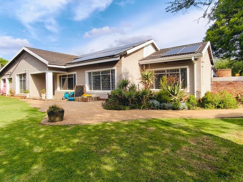 Rear view of a well-maintained house featuring a paved patio, landscaped garden, and roof-mounted solar panels.