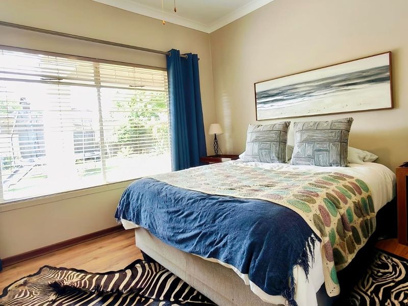 A well-lit bedroom featuring laminate flooring, a ceiling fan, and large windows with venetian blinds, offering a comfortable and functional living space.