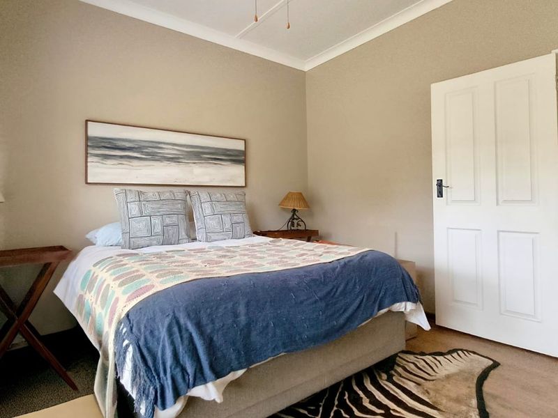A well-proportioned bedroom featuring neutral wall tones, classic cove cornicing, and a traditional panelled door leading to an adjacent space.