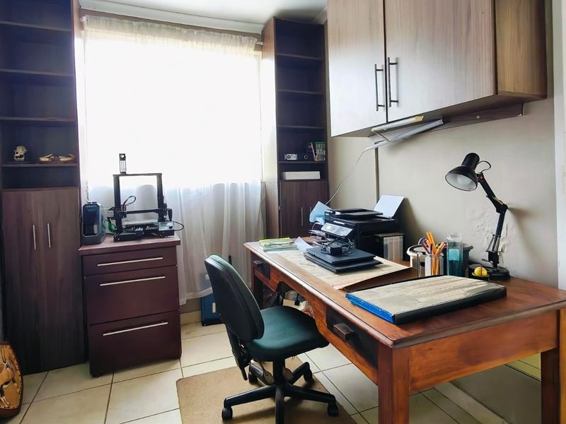 A functional home office space featuring built-in wooden cabinetry, tiled flooring, and a window providing natural light.
