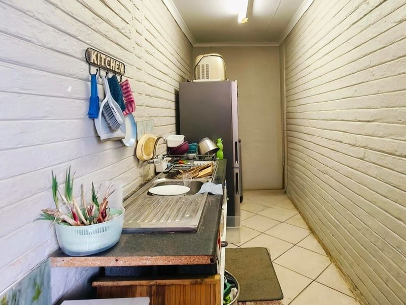 A functional scullery area featuring a stainless steel sink, tiled flooring, and painted brick walls, providing additional prep and wash-up space.