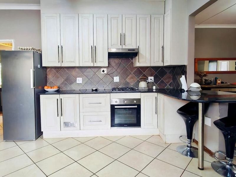 A functional kitchen featuring light-toned cabinetry, granite countertops, a gas hob with extractor, and a breakfast bar, finished with tiled flooring.