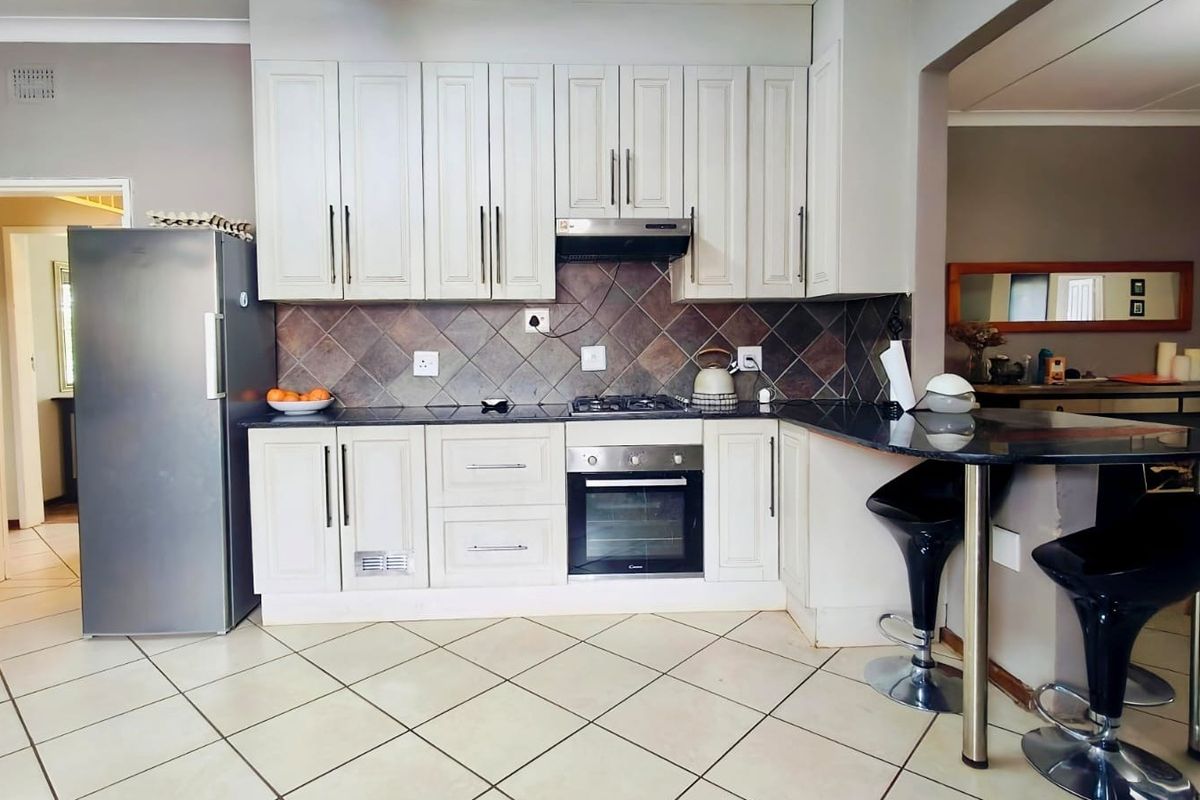 A functional kitchen featuring light-toned cabinetry, granite countertops, a gas hob with extractor, and a breakfast bar, finished with tiled flooring.