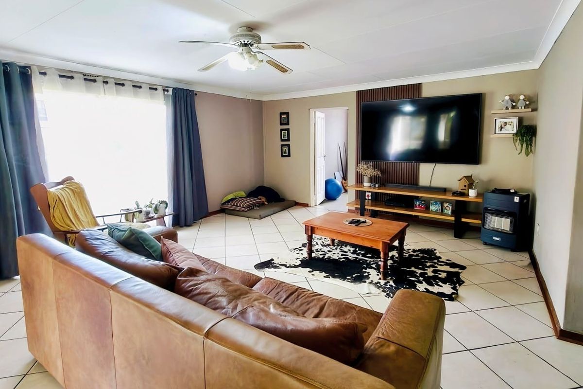 A spacious living room featuring tiled flooring, a ceiling fan, and a decorative slatted wood feature wall.