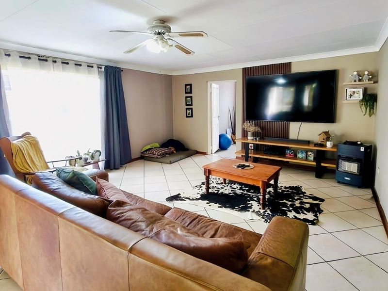 A spacious living room featuring tiled flooring, a ceiling fan, and a decorative slatted wood feature wall.