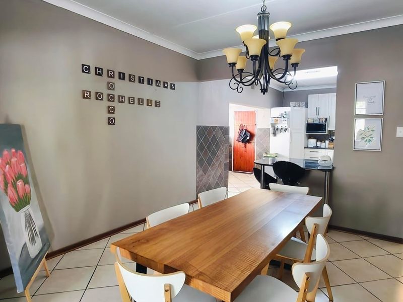 Open plan dining area featuring tiled flooring, a central chandelier, and a breakfast bar leading into the kitchen space.