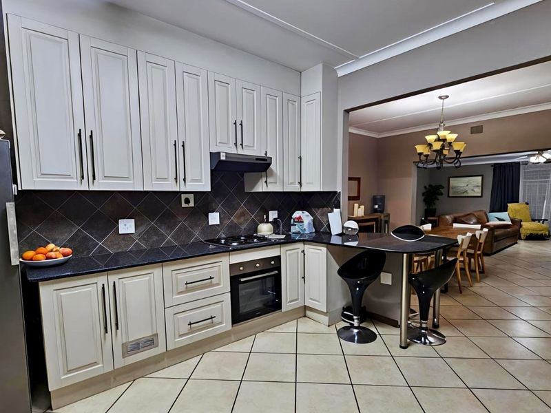 Open-plan kitchen featuring light-toned cabinetry, dark granite countertops, built-in oven and hob, and a breakfast bar flowing into the adjacent living and dining area.