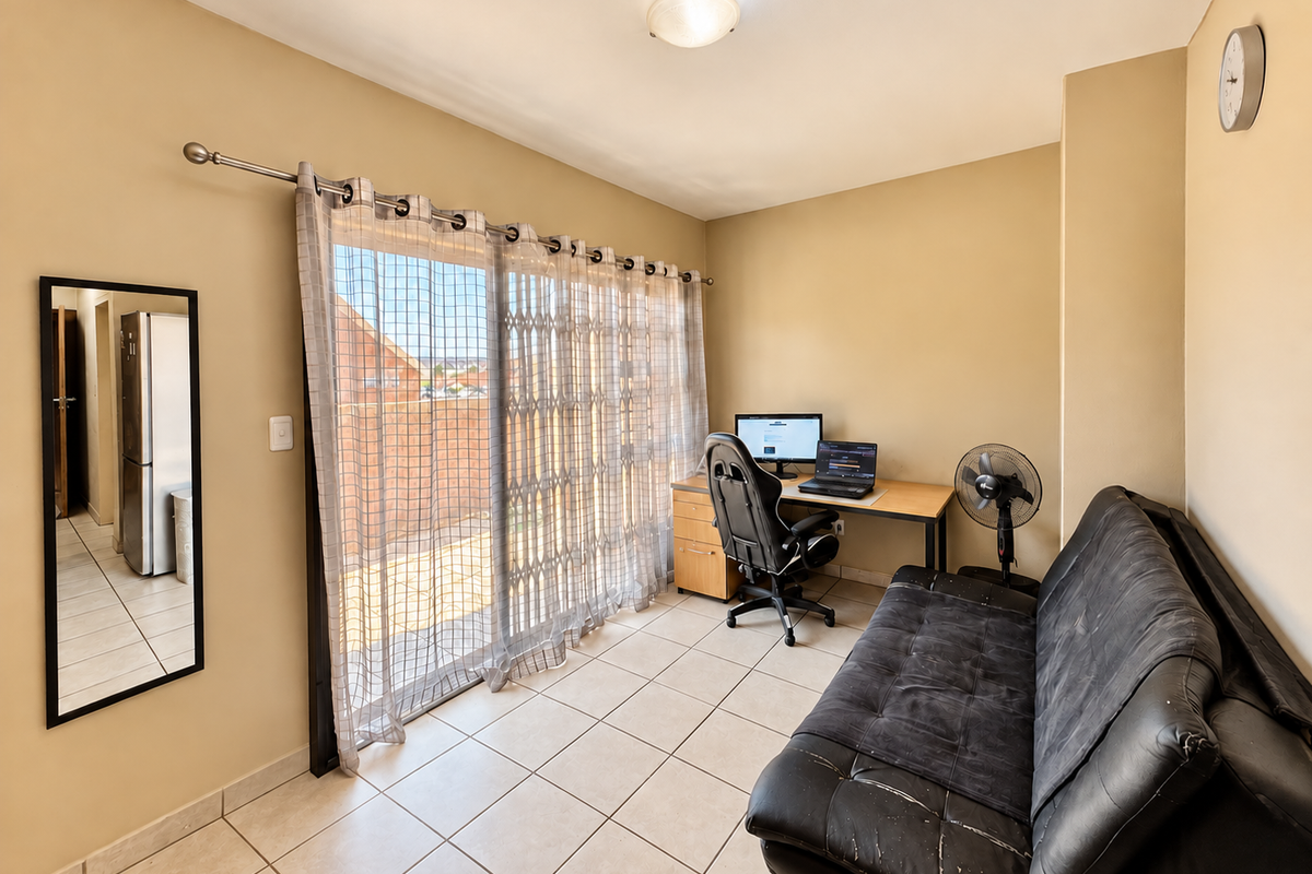 A functional living area featuring ceramic floor tiles and a large sliding glass door with a security gate, providing access to an outdoor space.