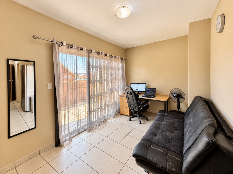 A functional living area featuring ceramic floor tiles and a large sliding glass door with a security gate, providing access to an outdoor space.