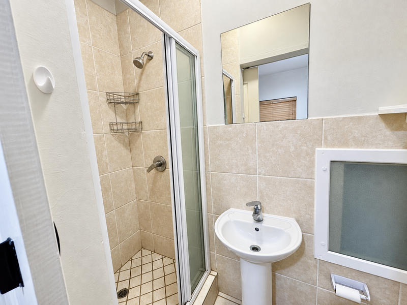 A clean, functional bathroom featuring a tiled shower enclosure, pedestal basin with mixer tap, and wall-mounted mirror.