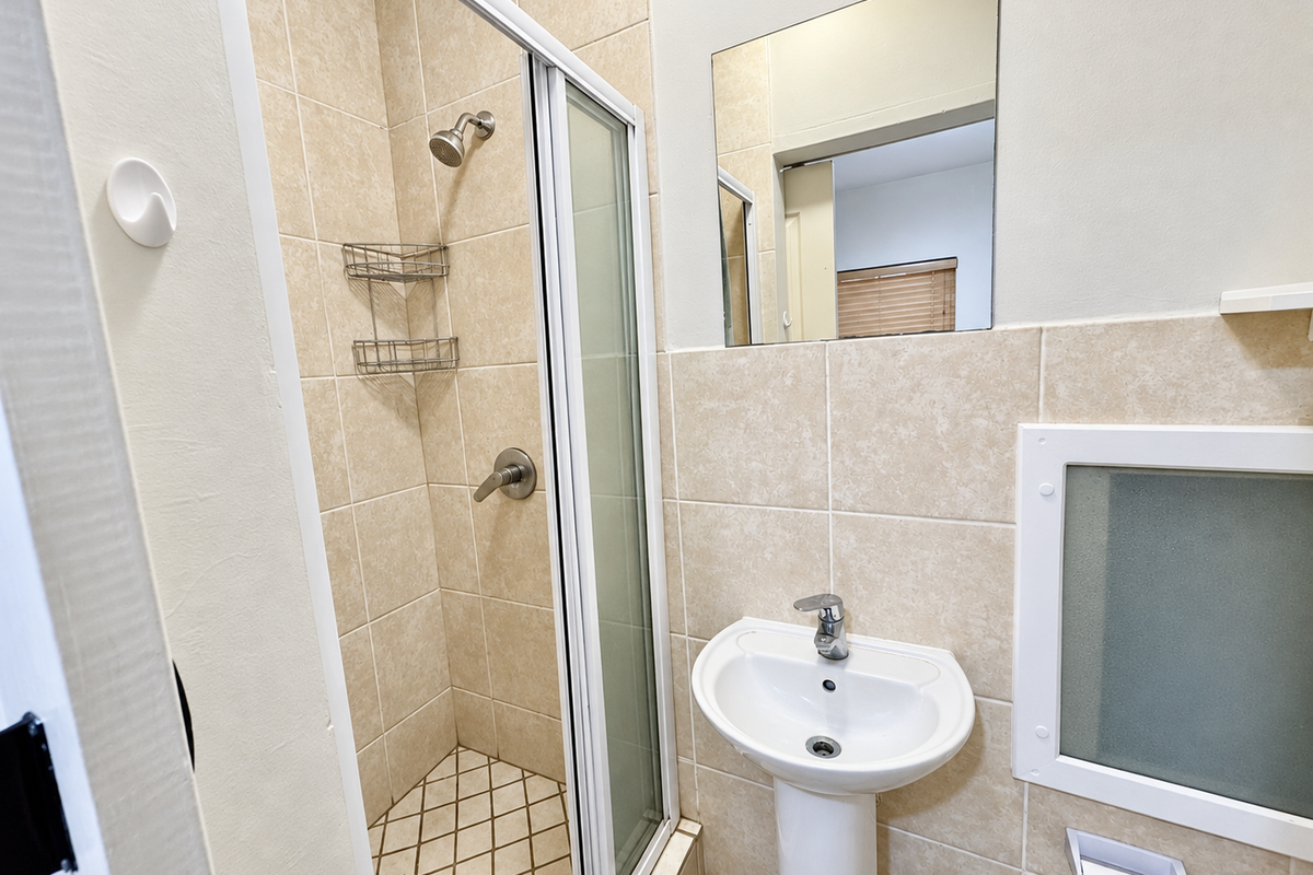 A clean, functional bathroom featuring a tiled shower enclosure, pedestal basin with mixer tap, and wall-mounted mirror.