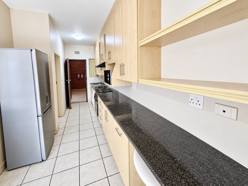 A functional kitchen featuring light wood cabinetry, dark granite countertops, a gas hob, and tiled flooring, offering ample storage and workspace.