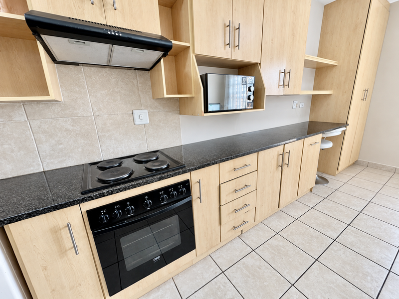 A functional kitchen featuring light wood cabinetry, granite countertops, a built-in oven, electric hob, and tiled flooring throughout.