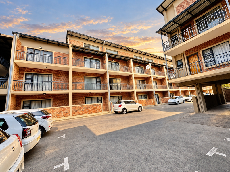 Exterior view of a multi-story apartment complex featuring brick facade, private balconies with metal railings, and dedicated paved parking spaces.