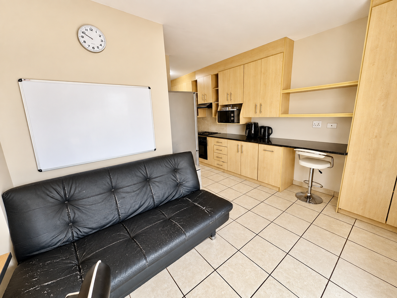 Open-plan living area featuring a functional kitchen with light wood cabinetry, black granite countertops, built-in oven, and tiled flooring throughout.