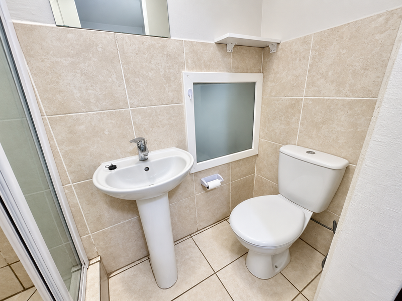 A compact bathroom featuring a pedestal basin, toilet, and shower enclosure with neutral wall and floor tiling.