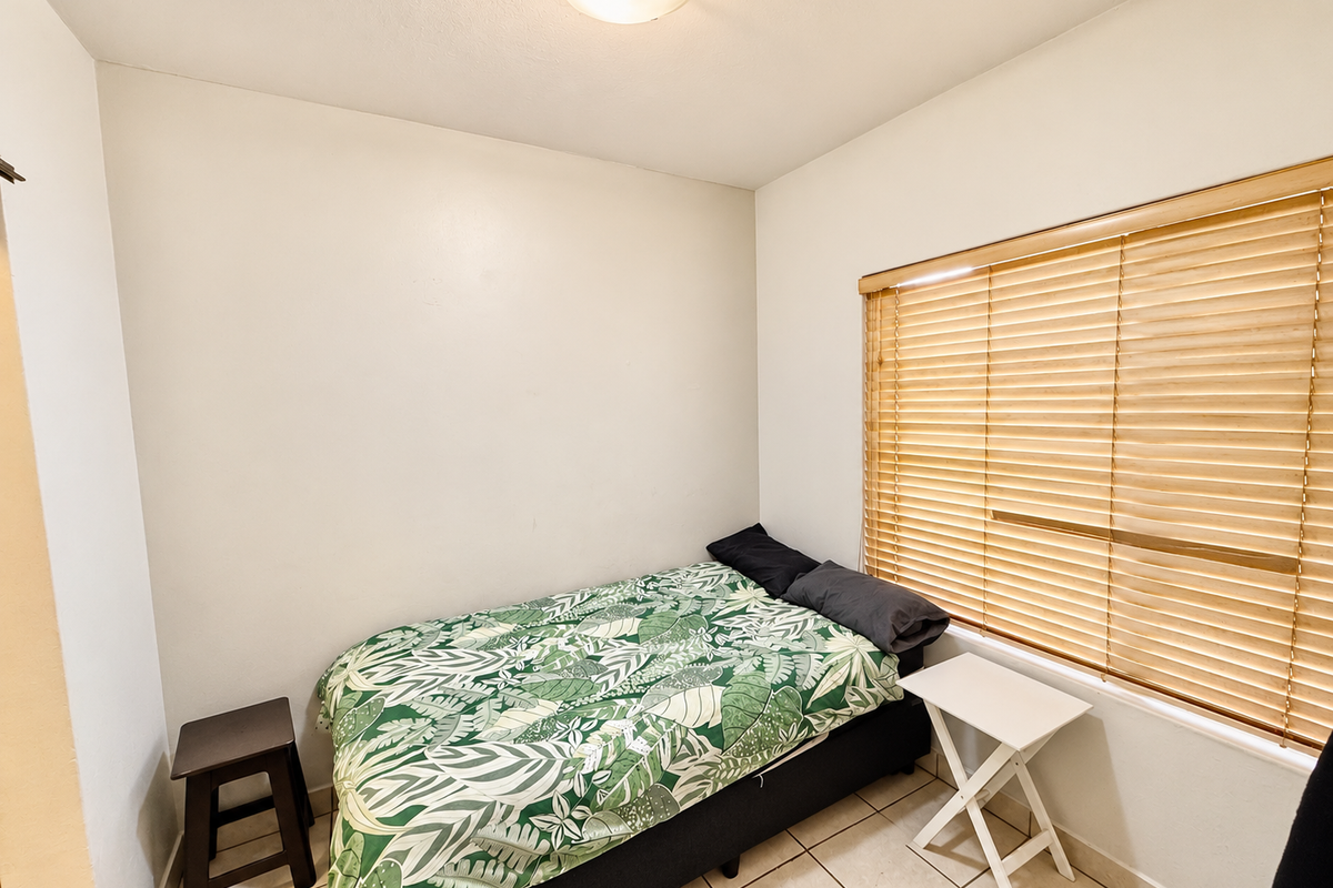 A compact bedroom featuring tiled flooring, neutral walls, and wooden venetian blinds, providing a functional and well-lit sleeping space.