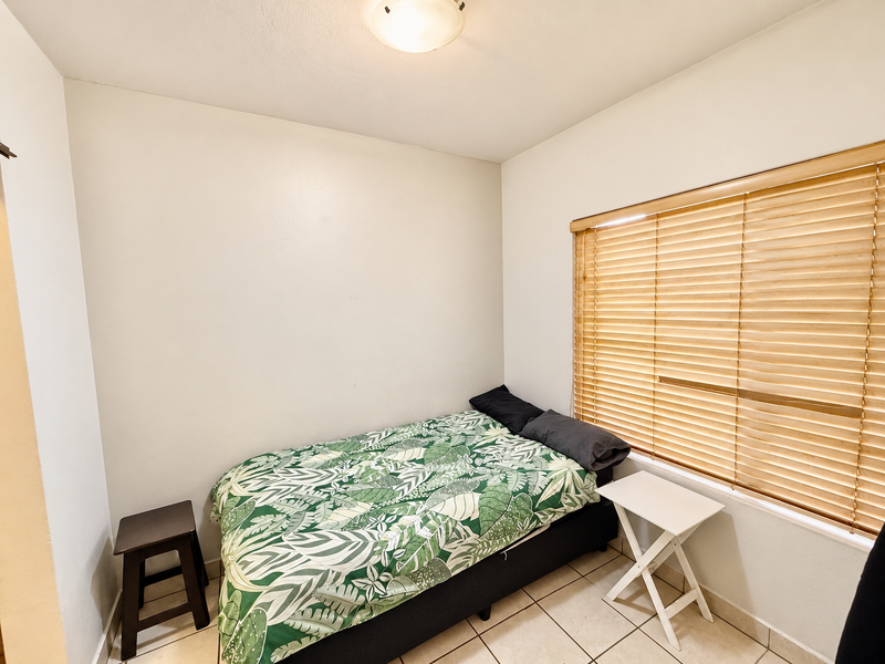 A compact bedroom featuring tiled flooring, neutral walls, and wooden venetian blinds, providing a functional and well-lit sleeping space.